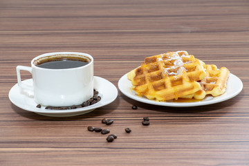 Viennese waffles sprinkled with powdered sugar and poured with honey with a cup of coffee.