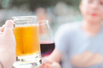 blurred hand holding beer mug smash with wine glass at restaurant, selective focus