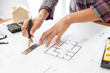 Construction and building concept. Engineers or architect holding a pen with drawings in construction on blueprints in office.
