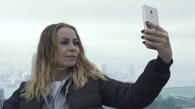 Happy travel girl taking mobile selfie Hong Kong city panorama. Tourist woman photographing selfie portrait by smartphone traveling in Victoria Peak in Hong Kong city. Tourism and travel lifestyle