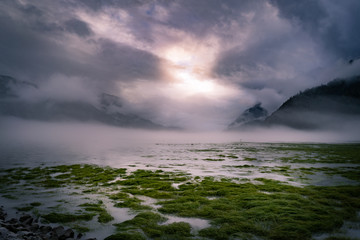 Ruhe vor dem Sturm Sonne scheint durch dichte Wolken in Bucht mit Nebel und Landschaft