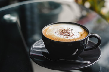 close up modern hot black coffee the cappuccino on dark background with coffee bubble foam pattern and texture in black cup looking and feel so delicious on glasses table in coffee shop.