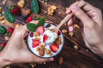 Health concept - Top view hands holding a spoon, yogurt and strawberry on a wooden table.