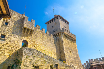 Fototapeta na wymiar Prima Torre Guaita first medieval tower with stone brick fortress wall with merlons on Mount Titano rock, blue sky white clouds copy space background, Republic San Marino