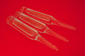 Three glass ampoules with a transparent solution close-up on a red background.