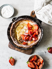 Dutch baby pancake dusted with powdered sugar with fresh strawberries in a black frying pan