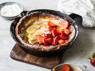 Dutch baby pancake dusted with powdered sugar with fresh strawberries in a black frying pan