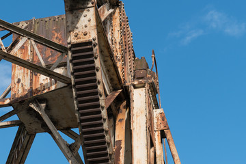 Weathered, rusty loading crane in abandoned dock. Shot from below against blue sky