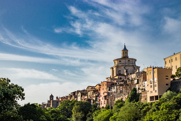 Fototapeta na wymiar A view of the city of Zagarolo, with the houses built sheer above a tuff hill. Above the roofs the dome of the church of San Pietro appears. The valley full of trees. Province of Rome, Lazio