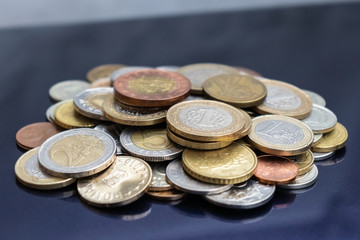 A small mountain of coins from different countries on a blue background. View closeup at an angle.