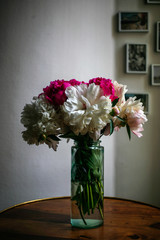 Gorgeous white and pink pions in a glass vase on the table with some light in front of the Parisian window