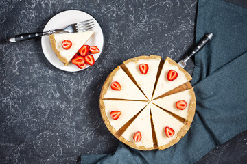 Homemade cheesecake with fresh strawberries sliced on black stone background