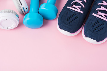 Female sport shoes, blue dumbbells andwhite headphones on a pink background with copy space, top view