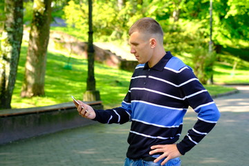 Young stylish man stay in a park and holding smartphone. Lifestyle Outdoor street photo