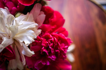 Gorgeous white and pink pions in a glass vase on the table with some petal in sunset light close up