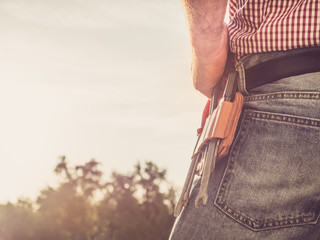 Male hand, blue jeans and vintage belt with tools in the park against the backdrop of green trees and of the rays the setting sun. Close-up. Concept of labor and employment