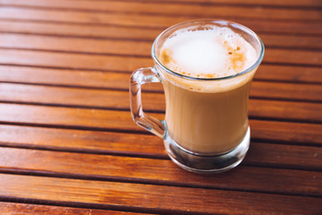 Cup or glass of coffee with white foam on wooden brown table, with copy space, top view