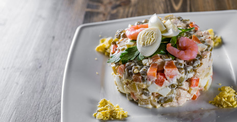 Olivier salad with shrimps, eggs and vegetables in a plate on wooden table