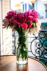 Gorgeous white and pink pions in a glass vase in sunset light in front of the open Parisian window