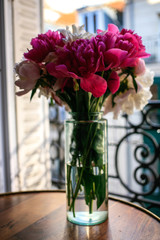 Gorgeous white and pink pions in a glass vase in sunset light in front of the open Parisian window