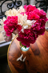 Gorgeous white and pink pions in a glass vase in sunset light in front of the open Parisian window top view