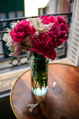 Gorgeous white and pink pions in a glass vase in sunset light in front of the open Parisian window
