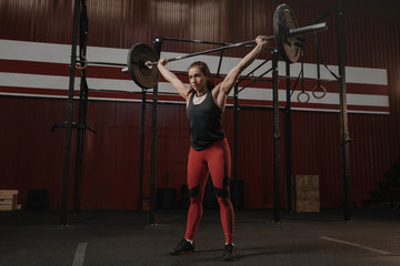 Fototapeta na wymiar Young strong woman holding heavy barbell overhead. Sports woman doing crossfit exercise.