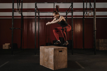 Fototapeta na wymiar Young crossfit woman doing box jumping at the gym.