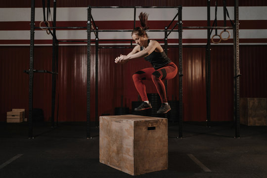 Young crossfit woman doing box jumping at the gym.