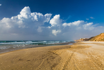Windy sunny day on the beach. Stormy sea, strong wind, white foam on the waves. Netanya, Israel, Mediterranean sea. Swimming is  prohibited. Nobody on the beach, just footprints on the wet sand.