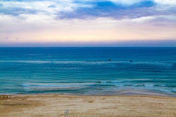 Twilight time and sunset at the beach in Netanya, Israel, Mediterranean sea. Overcast sky, foam and waves. Aerial view. 2 boats in the sea.