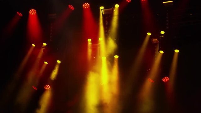 Red and yellow spotlights flash in the fog at a rock concert in the dark. Stage lighting and smoke machine. Background for show or event presentation.