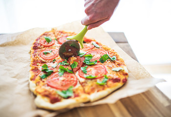 high angle view of hand cutting delicious homemade pizza Margherita with tomatoes and basil using a...