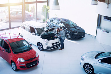Vehicle dealer presenting new car to the buyer at automobile showroom.