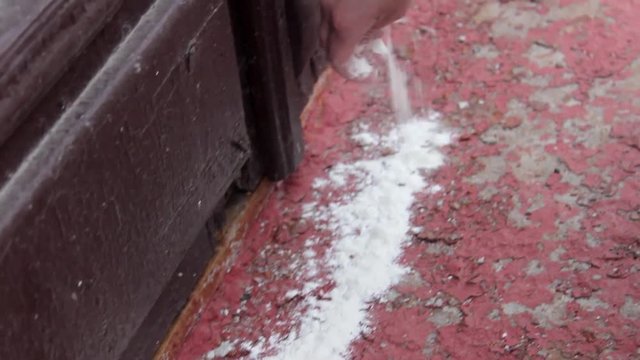 Hand pours white powder on the threshold of the house