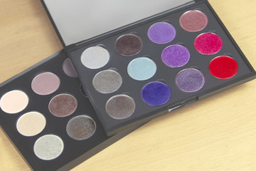 Two big eye shadow palettes of many colors shades in neutral. taupe and bright lilac, violet and red tones, one above another one. Indoors, light wooden background, close up, copy space.