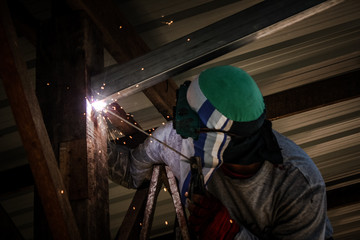 The welder is welding steel to make the garage roof. Industrial Worker at the factory welding closeup. Electric wheel grinding on steel structure in factory.