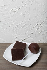 Chocolate cake pops and pieces of black chocolate on a white plate. On the surface covered with white decorative plaster.