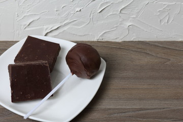Chocolate cake pops and pieces of black chocolate on a white plate. On the surface covered with white decorative plaster.