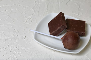 Chocolate cake pops and pieces of black chocolate on a white plate. On the surface covered with white decorative plaster.