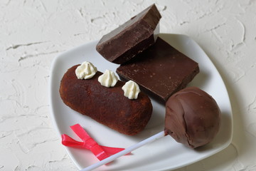 Chocolate cake pops and pieces of black chocolate on a white plate. Next to the potato cake. On the surface covered with white decorative plaster.