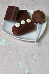 Chocolate cake pops and pieces of black chocolate on a white plate. Next to the potato cake. On the surface covered with white decorative plaster.