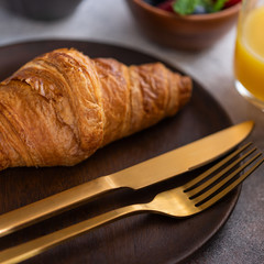 French croissant on wooden plate with gold cutlery. Typical  breakfast in yhe hotel.