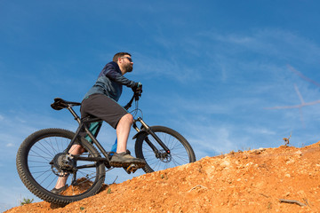 Obraz premium Cyclist in shorts and jersey on a modern carbon hardtail bike with an air suspension fork rides off-road on the orange-red hills at sunset evening in summer 
