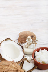 Background of coconut, coconut shell, oil in clay bowl and glass jar on white wooden table