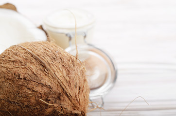 Coconut oil in airtight glass jar and shell pieces on white wooden table closeup