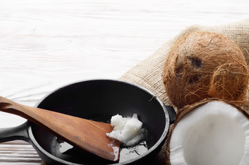 Coconut, shell with meat, cast iron skillet and spatula on hemp sackcloth on white wooden kitchen...