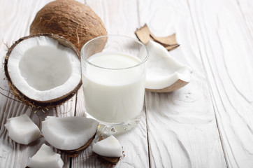 Drinking glass of milk or yogurt on blue napkin on white wooden table with coconut aside