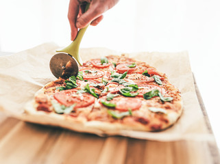 high angle view of hand cutting delicious homemade pizza Margherita with tomatoes and basil using a...