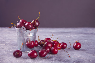ripe fresh cherry berries in small metal bucket on a concrete background close-up.